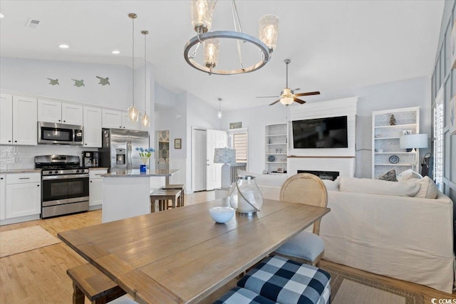 dining room featuring high vaulted ceiling, ceiling fan with notable chandelier, and light hardwood / wood-style floors