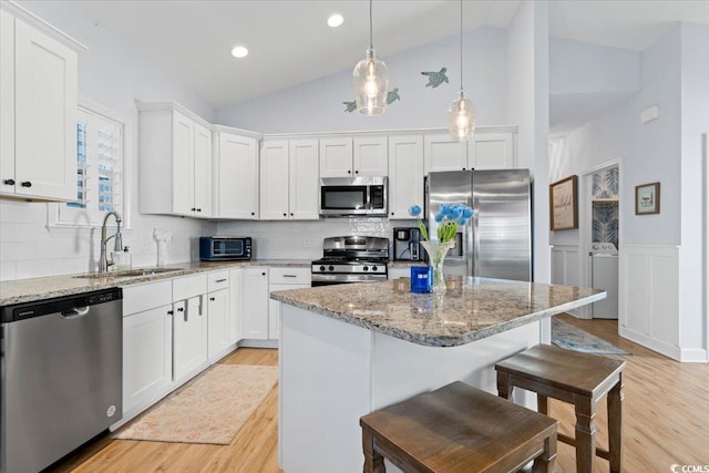 kitchen featuring sink, appliances with stainless steel finishes, light stone countertops, white cabinets, and a kitchen island