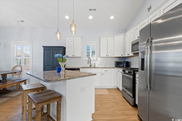 kitchen with stone counters, appliances with stainless steel finishes, sink, white cabinets, and a center island