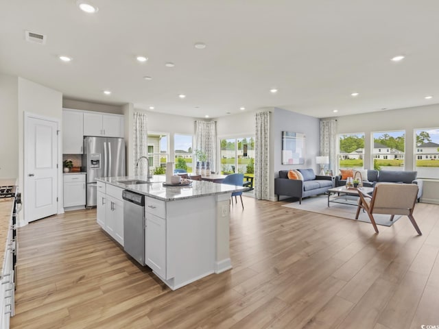 kitchen featuring sink, stainless steel appliances, light stone countertops, an island with sink, and white cabinets