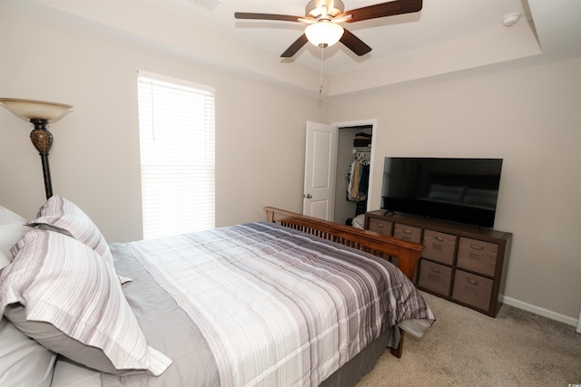 bedroom with a raised ceiling, light colored carpet, ceiling fan, and a closet