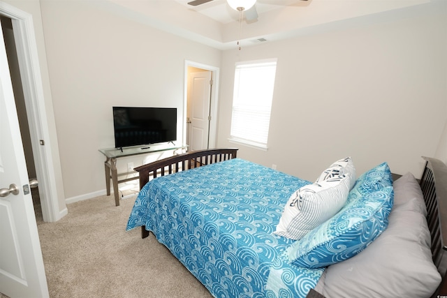 bedroom with a raised ceiling, light colored carpet, and ceiling fan