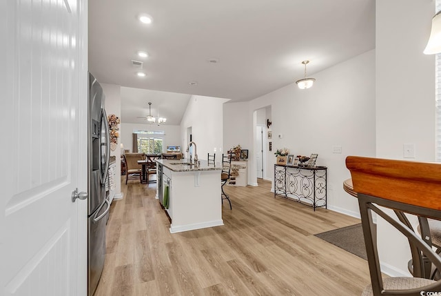 kitchen featuring hanging light fixtures, light hardwood / wood-style floors, an island with sink, and stainless steel refrigerator with ice dispenser