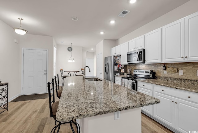 kitchen featuring an island with sink, stainless steel appliances, sink, and hanging light fixtures