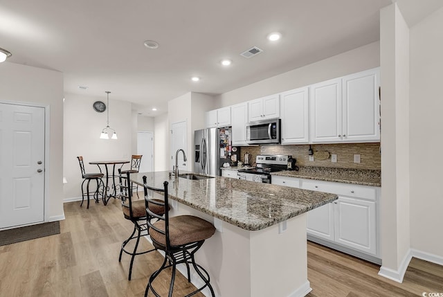 kitchen with stone countertops, a kitchen island with sink, white cabinets, and appliances with stainless steel finishes