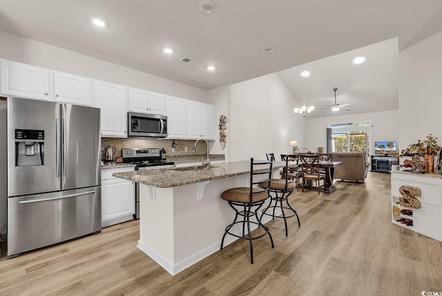 kitchen with stone counters, white cabinetry, sink, stainless steel appliances, and a center island with sink