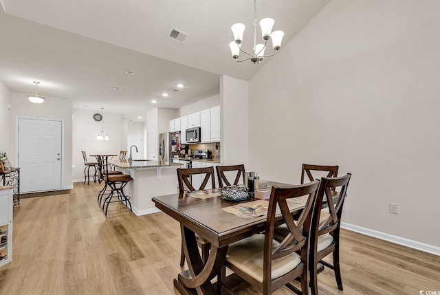 dining area with sink, light hardwood / wood-style flooring, and a notable chandelier