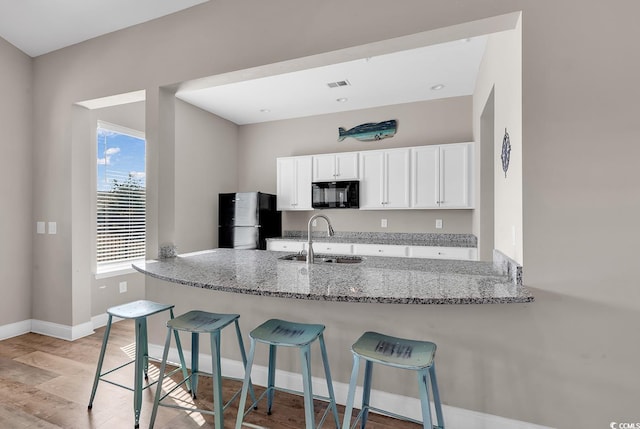 kitchen featuring sink, light stone counters, black appliances, white cabinets, and kitchen peninsula