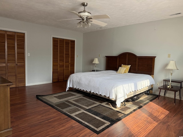 bedroom featuring ceiling fan, two closets, dark hardwood / wood-style floors, and a textured ceiling