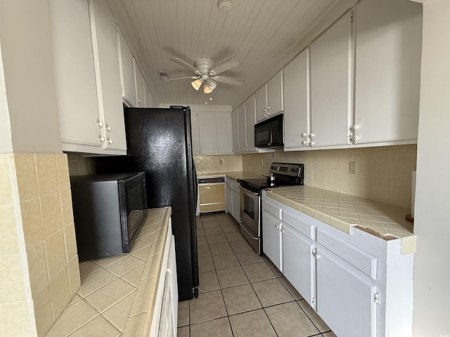 kitchen with light tile patterned floors, ceiling fan, stainless steel range with electric stovetop, tile counters, and white cabinets