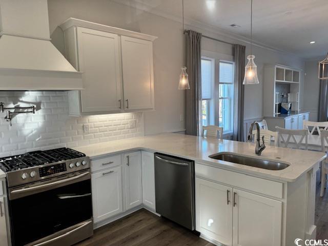 kitchen with a sink, appliances with stainless steel finishes, a peninsula, custom exhaust hood, and white cabinets