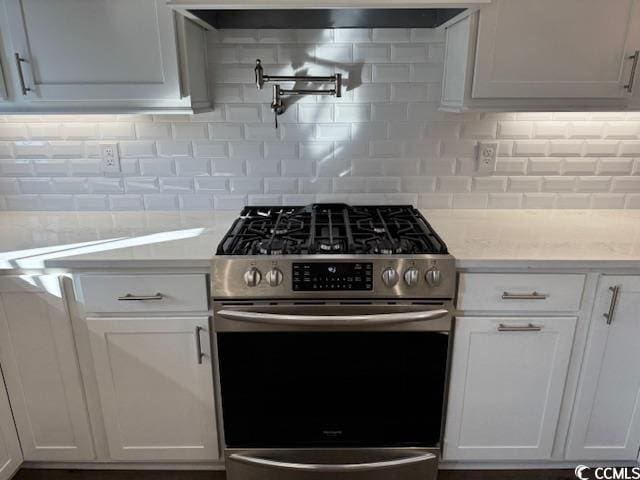 kitchen with white cabinets, gas stove, light stone counters, and tasteful backsplash