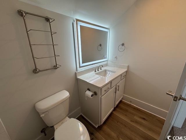 half bathroom featuring baseboards, toilet, vanity, and wood finished floors