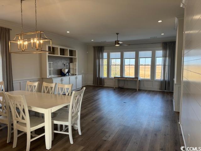 unfurnished dining area with ceiling fan with notable chandelier, a decorative wall, crown molding, and dark wood finished floors