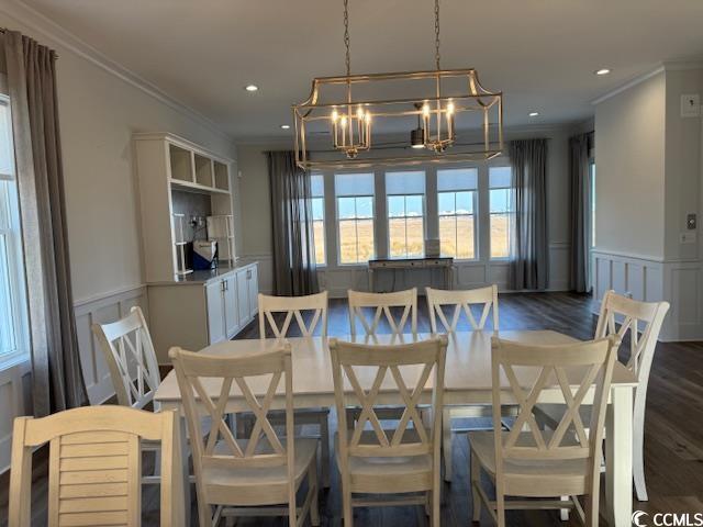 dining room with a wainscoted wall, dark wood-style floors, crown molding, and a chandelier