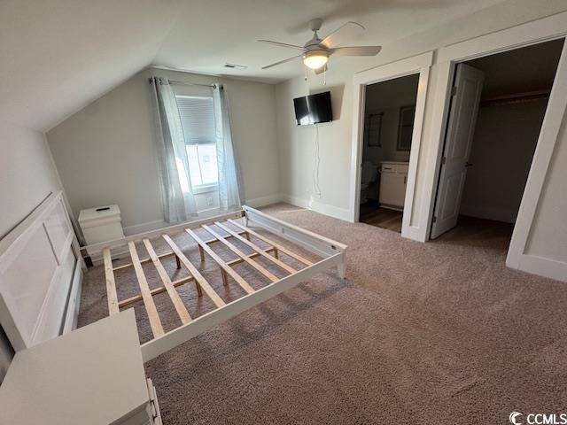 unfurnished bedroom with dark carpet, ensuite bath, lofted ceiling, ceiling fan, and a walk in closet