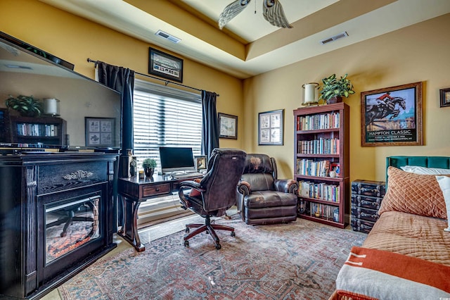 carpeted office space featuring a raised ceiling and ceiling fan