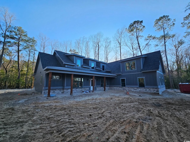 rear view of property featuring stone siding and roof with shingles