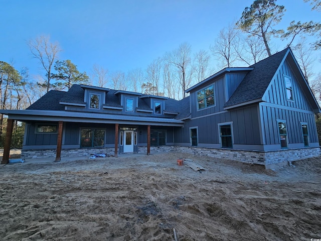 back of property with stone siding, roof with shingles, and board and batten siding