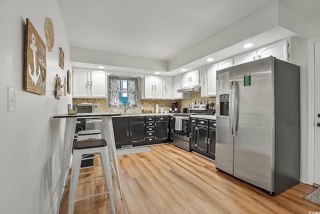 kitchen featuring appliances with stainless steel finishes, sink, white cabinets, decorative backsplash, and light hardwood / wood-style flooring