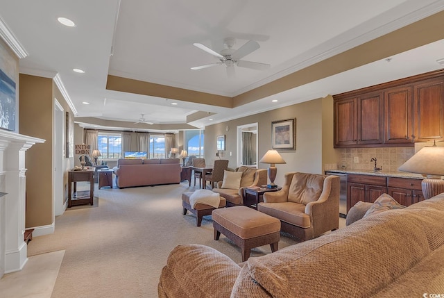 living area with light colored carpet, a ceiling fan, recessed lighting, a tray ceiling, and ornamental molding
