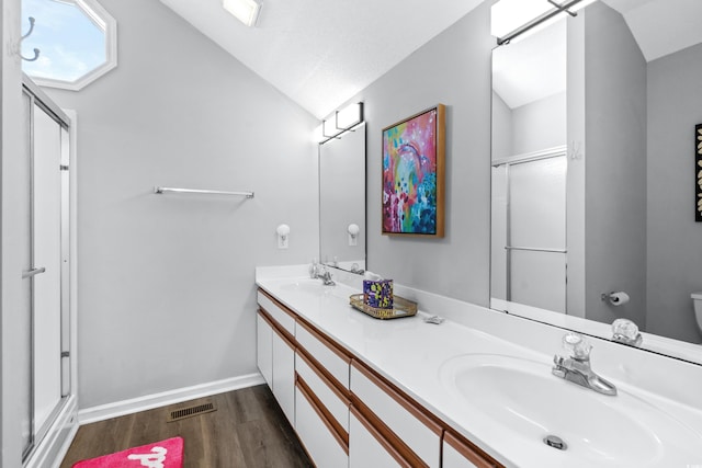 bathroom with a shower with door, vaulted ceiling, hardwood / wood-style floors, and vanity