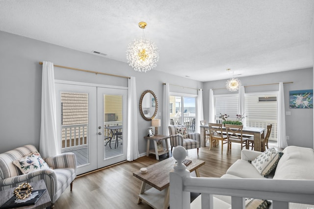 living room featuring hardwood / wood-style floors, a textured ceiling, a chandelier, and french doors