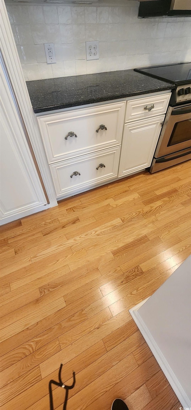 details with tasteful backsplash, dark stone countertops, stainless steel electric stove, light hardwood / wood-style floors, and white cabinets