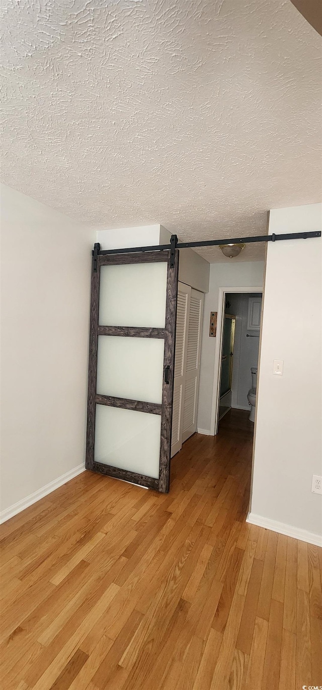 unfurnished room featuring hardwood / wood-style flooring, a barn door, and a textured ceiling