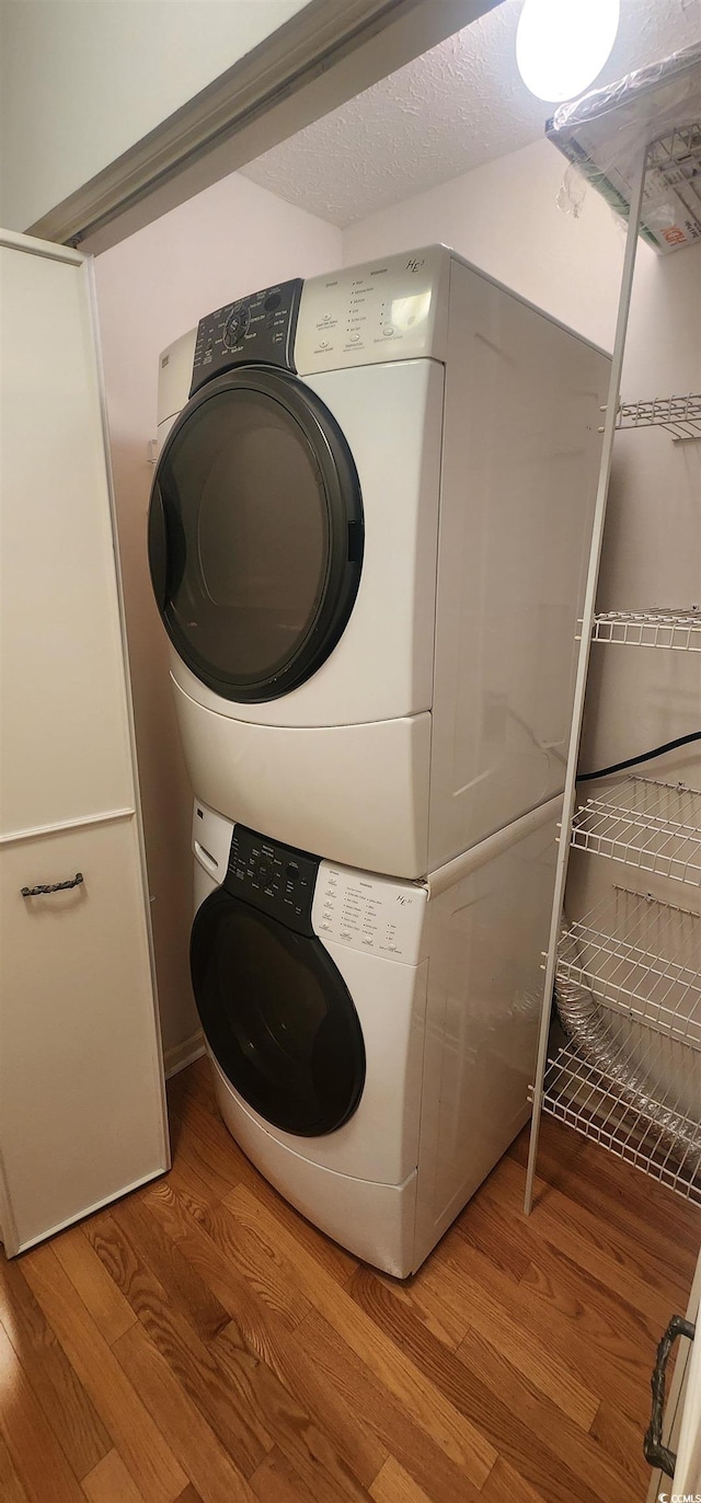 clothes washing area with hardwood / wood-style floors, stacked washer and clothes dryer, and a textured ceiling