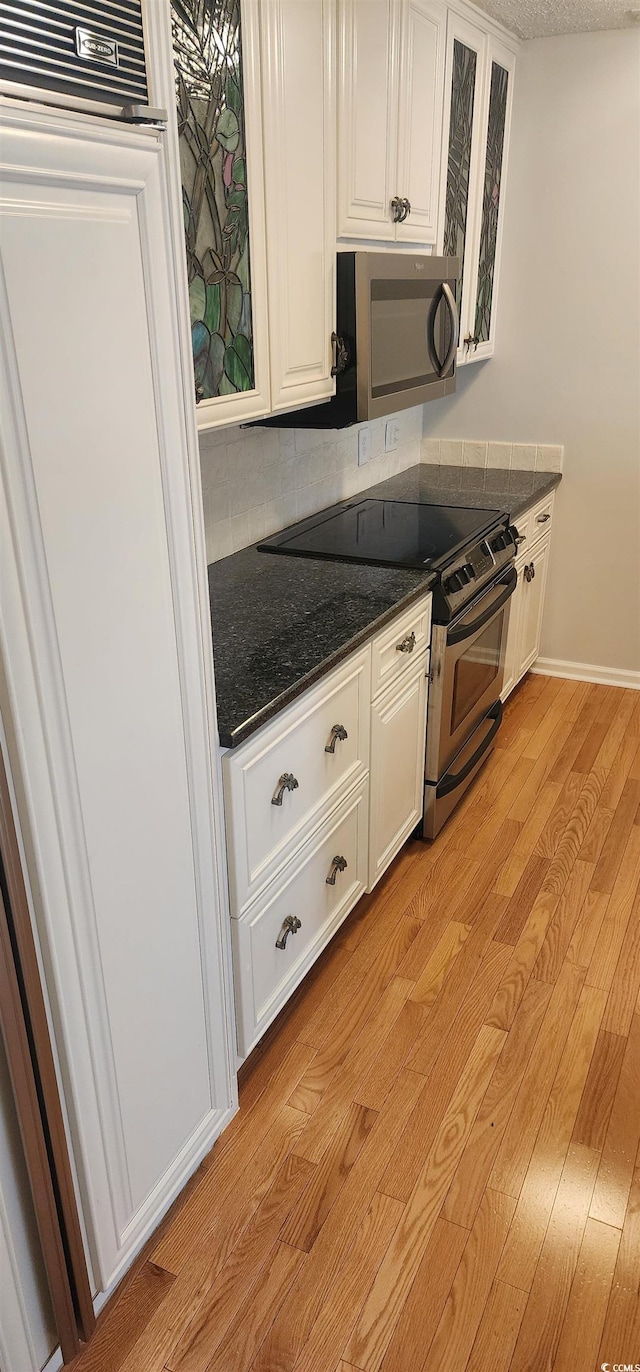 kitchen featuring white cabinetry, appliances with stainless steel finishes, dark stone countertops, and light wood-type flooring