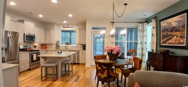 kitchen with hanging light fixtures, light wood-type flooring, a kitchen island, stainless steel appliances, and white cabinets