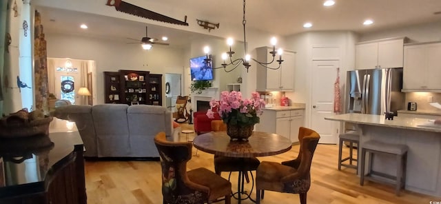 dining area with ceiling fan with notable chandelier and light hardwood / wood-style flooring