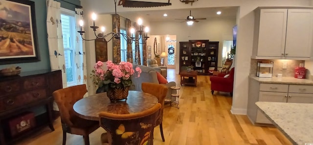 dining space with ceiling fan with notable chandelier and light hardwood / wood-style floors