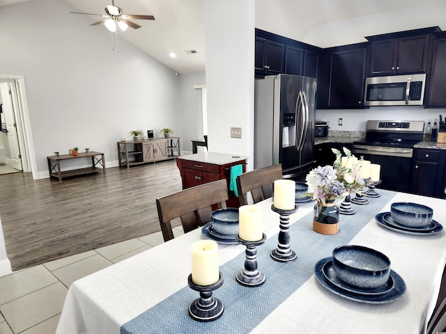 kitchen with tile patterned flooring, stainless steel appliances, a center island, high vaulted ceiling, and light stone countertops