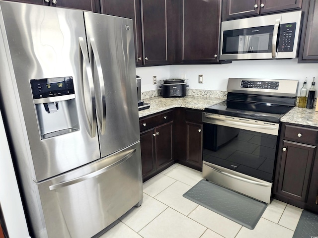 kitchen with light stone counters, stainless steel appliances, dark brown cabinets, and light tile patterned floors