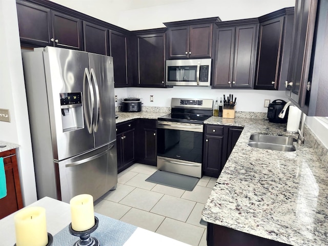 kitchen with light stone counters, dark brown cabinetry, appliances with stainless steel finishes, and light tile patterned floors