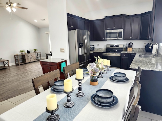 kitchen with light tile patterned flooring, sink, a center island, stainless steel appliances, and light stone countertops