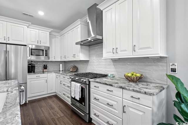 kitchen with wall chimney exhaust hood, premium appliances, dark hardwood / wood-style floors, light stone countertops, and white cabinets