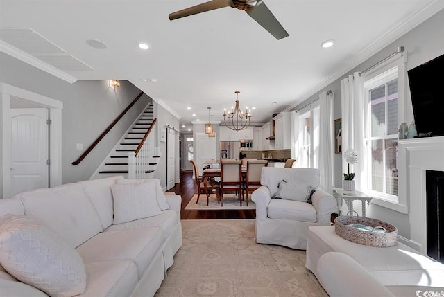 living room featuring ceiling fan with notable chandelier, ornamental molding, and light wood-type flooring