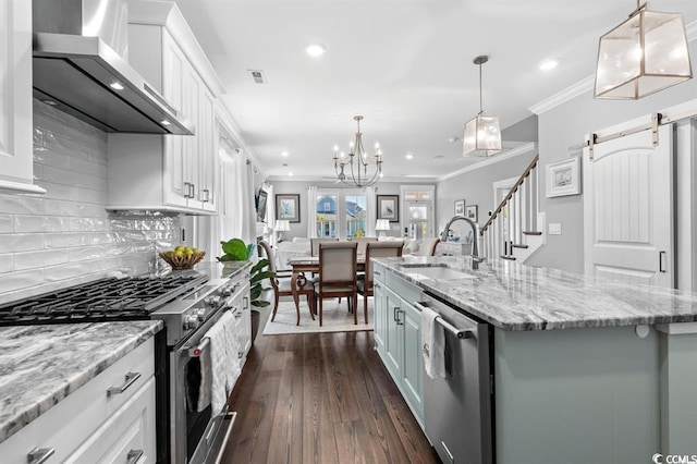 kitchen featuring wall chimney range hood, stainless steel appliances, white cabinets, and a center island with sink