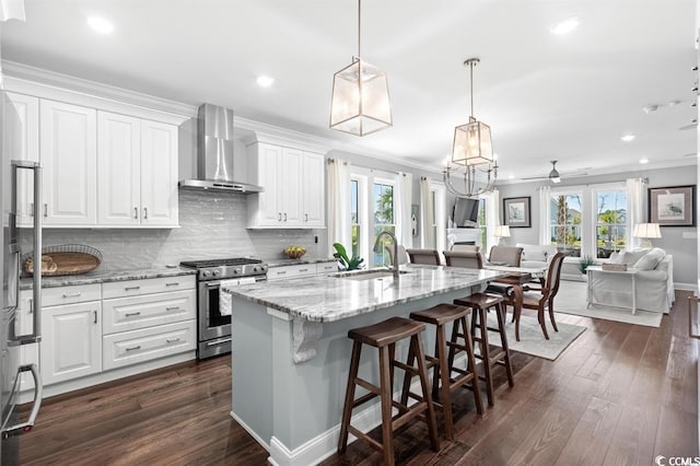 kitchen featuring pendant lighting, sink, white cabinets, stainless steel gas range oven, and wall chimney exhaust hood