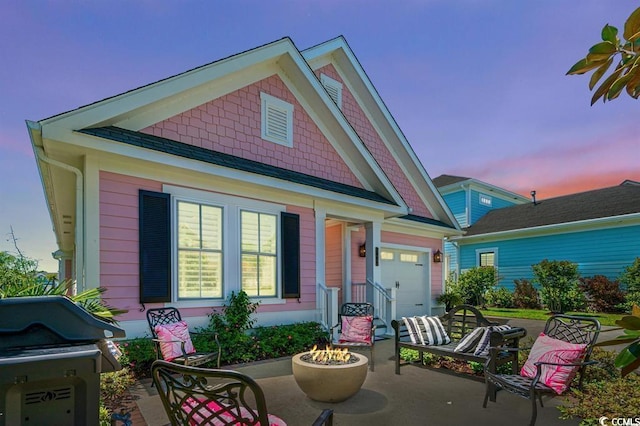 back house at dusk featuring a garage and a fire pit