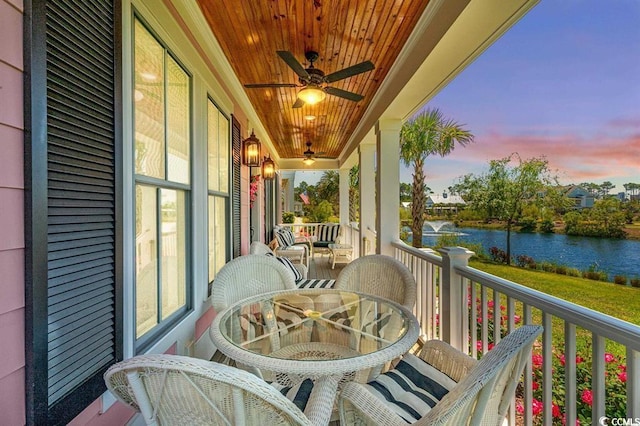 balcony at dusk featuring ceiling fan and a water view