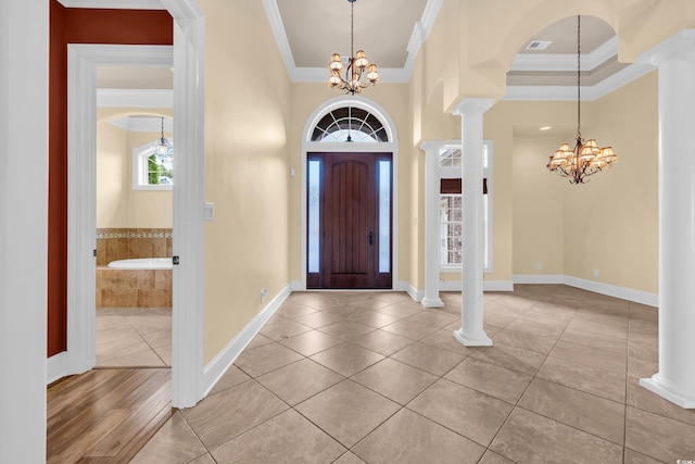 tiled foyer featuring a notable chandelier, ornamental molding, and ornate columns