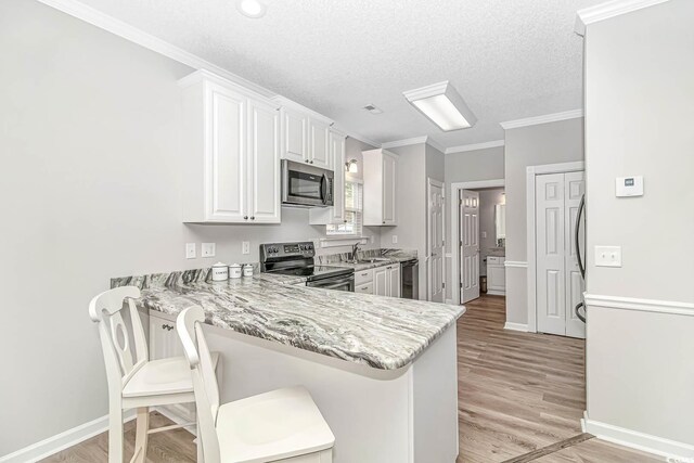 6001-1383 S Kings Hwy, Myrtle Beach, SC 29575 - kitchen with ornamental molding, a peninsula, white cabinets, light wood-style flooring, and appliances with stainless steel finishes