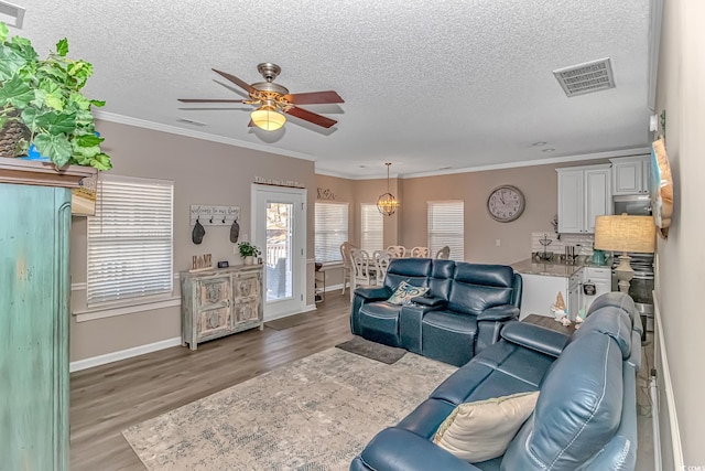 living area featuring light wood-style flooring, visible vents, a textured ceiling, and ornamental molding