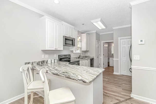 kitchen featuring a peninsula, white cabinetry, ornamental molding, appliances with stainless steel finishes, and light wood-type flooring