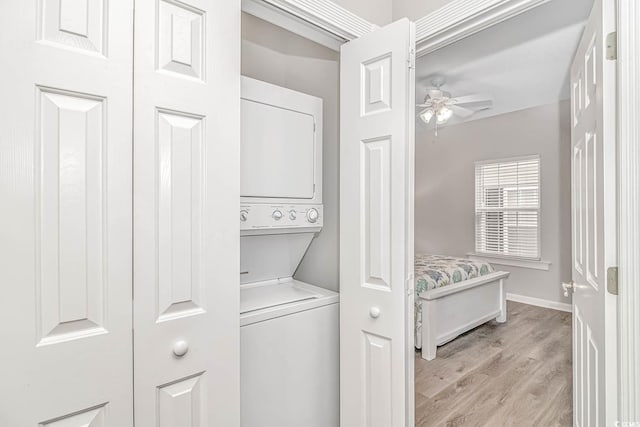 laundry area with ceiling fan, laundry area, stacked washer / dryer, baseboards, and light wood-style floors