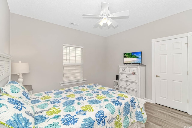 bedroom with light wood finished floors, a ceiling fan, visible vents, and a textured ceiling